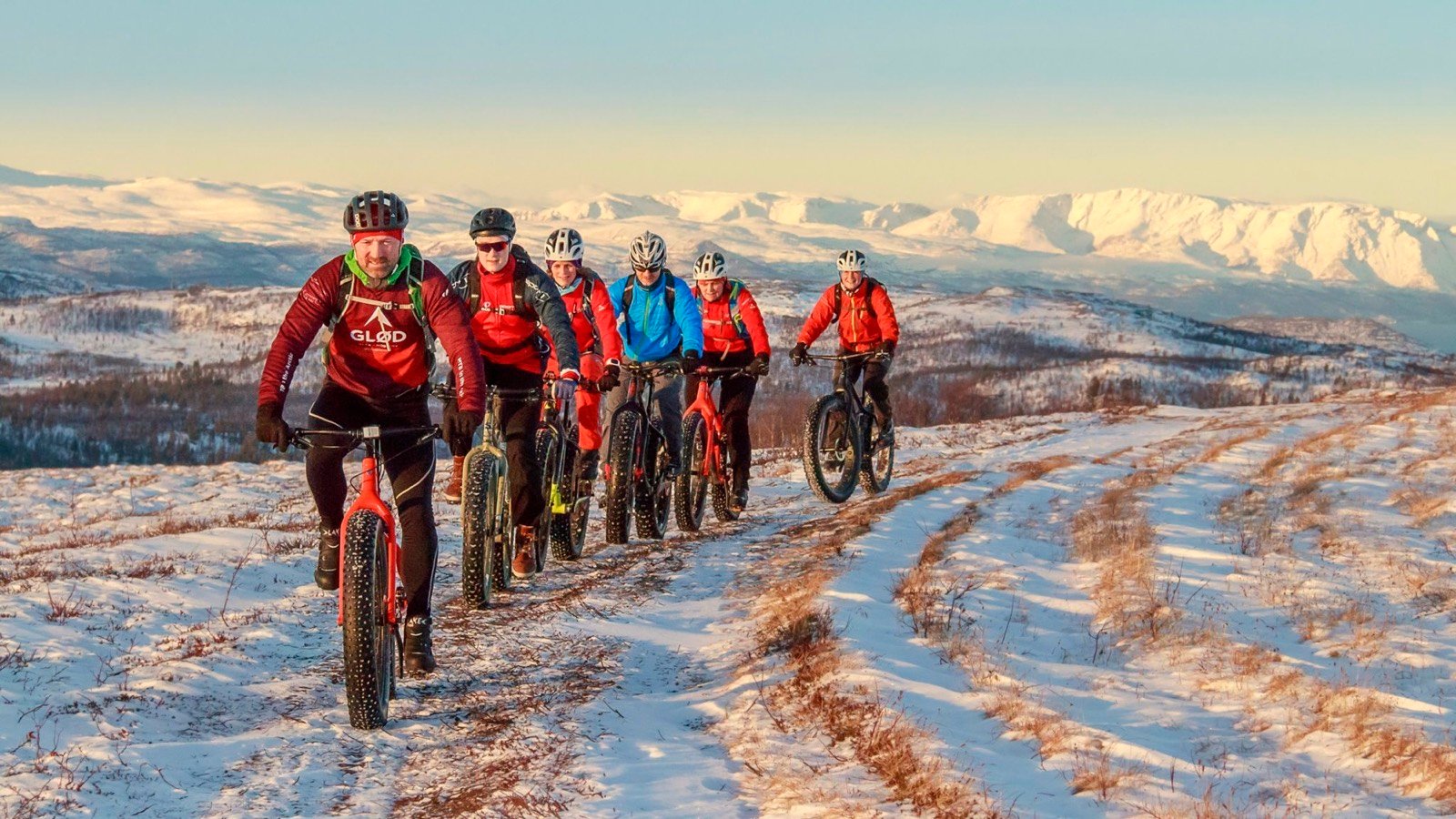 A group of fatbikers on a snowy trail in low winter sun