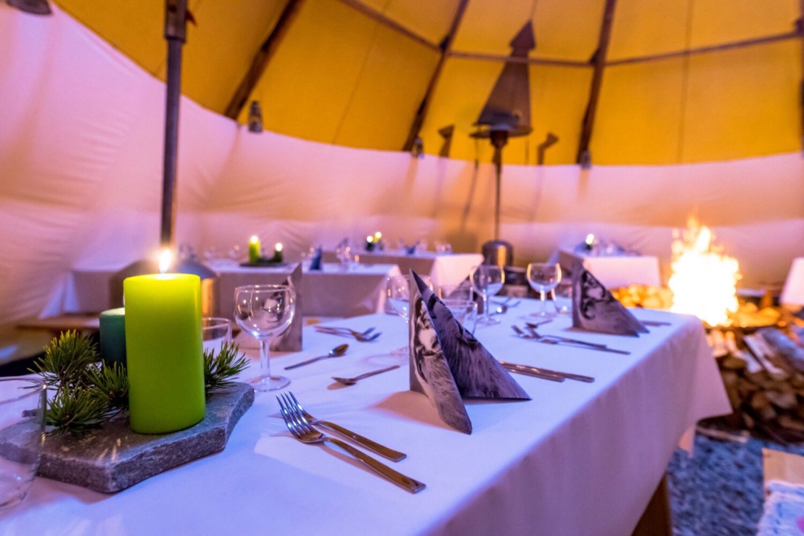 A candlelit table laid for dinner inside the large lavvu