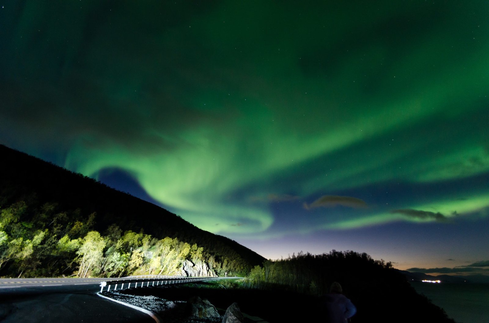 Northern Lights over a winding road and dark hills