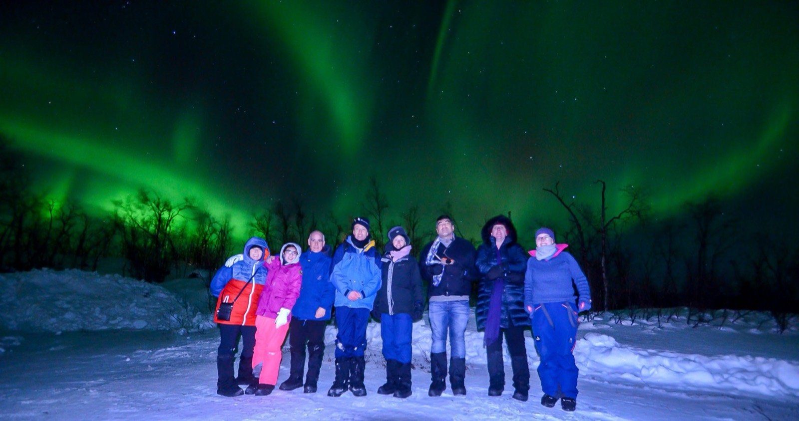 A small group of guests posing under green Northern Lights