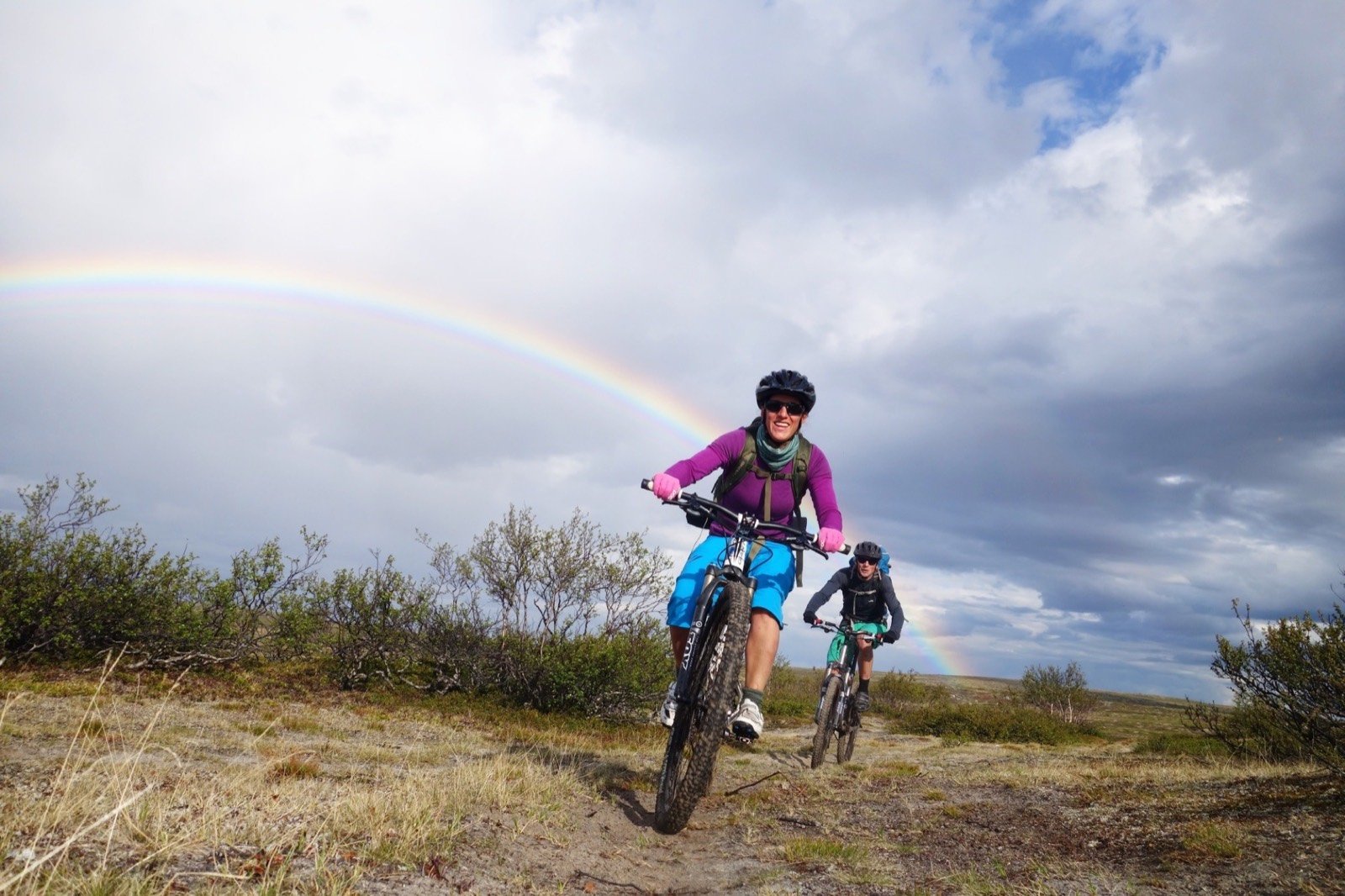 A mountain biker on a gravel trail under a rainbow
